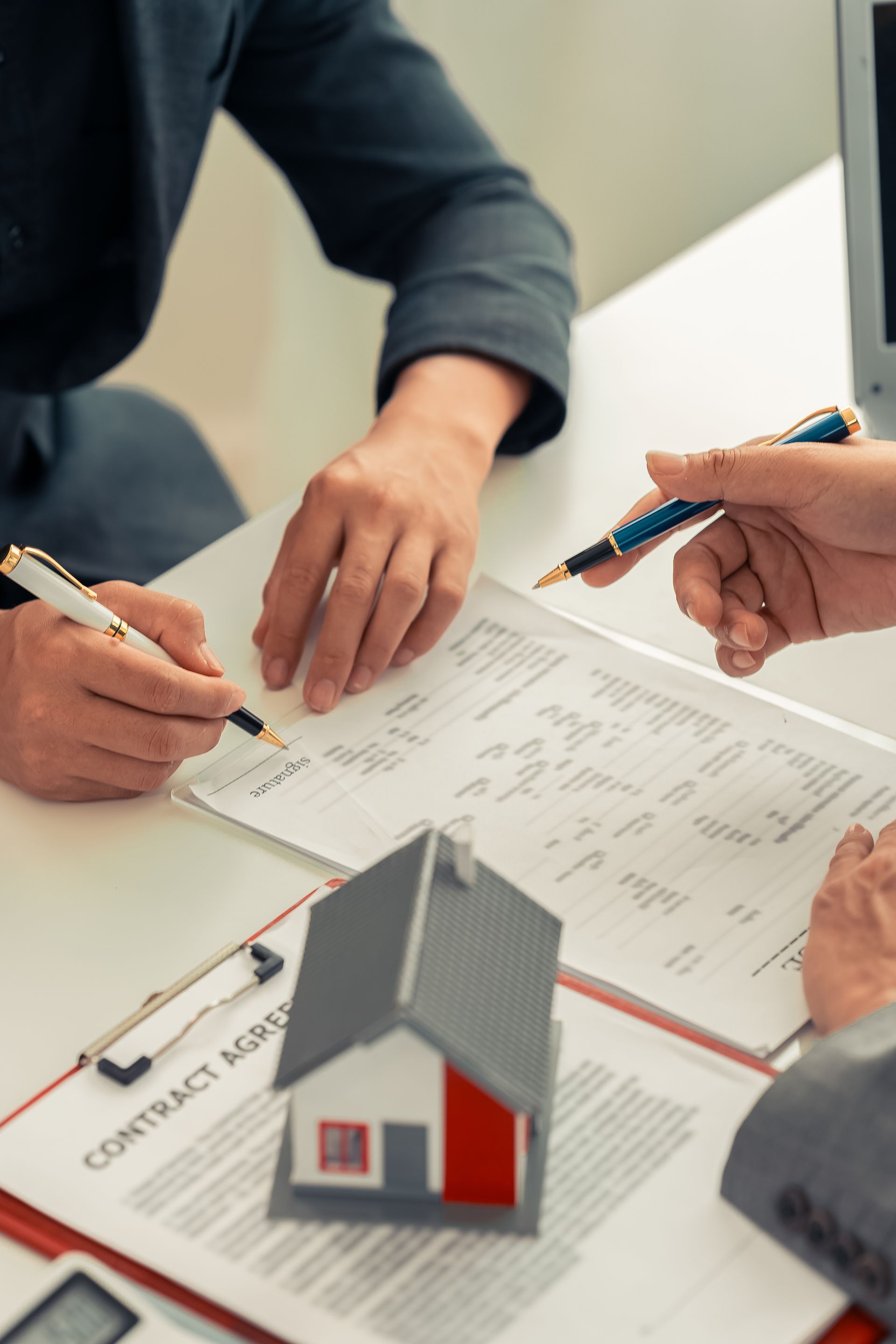 People signing a contract over a miniature house, on a desk.