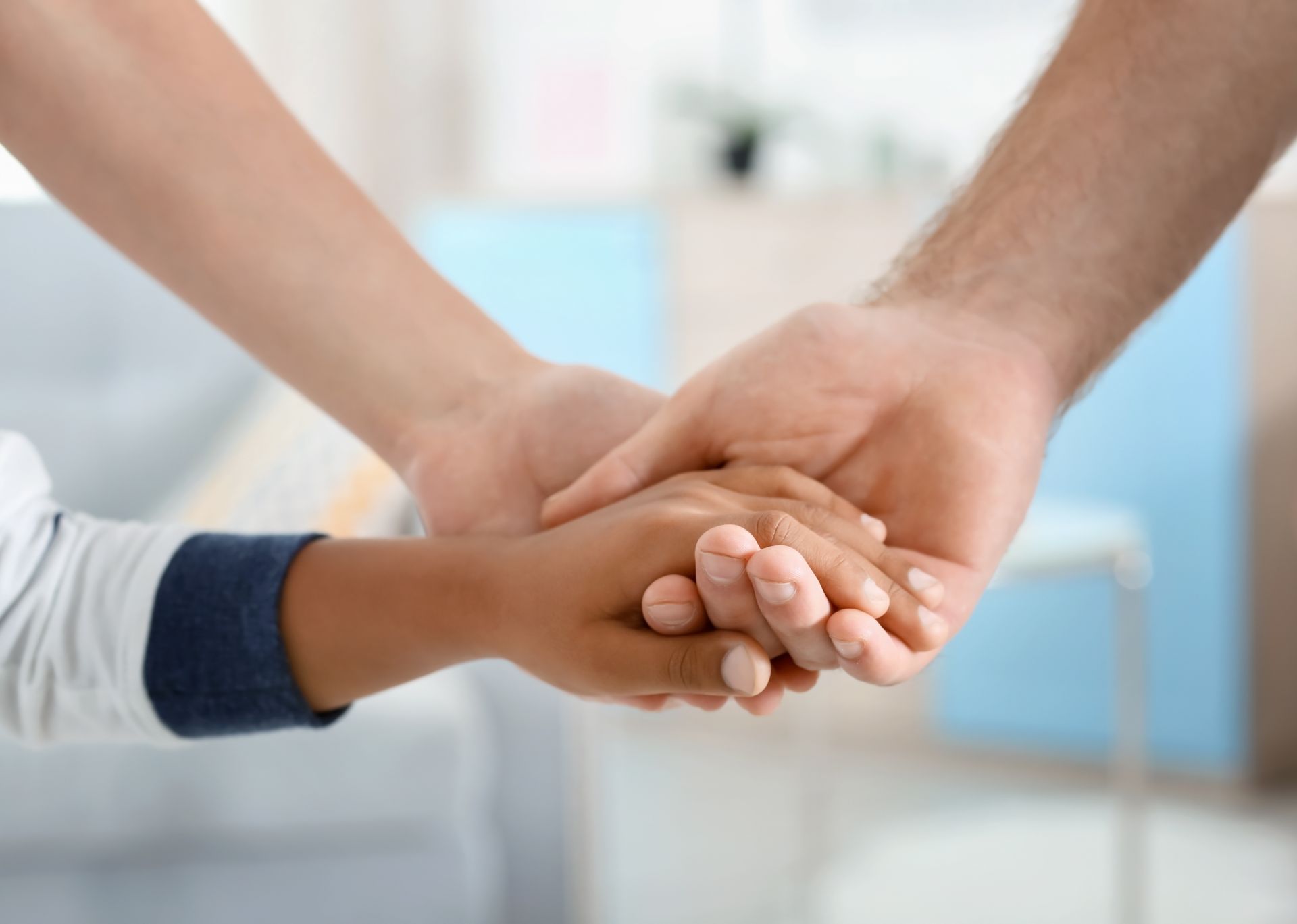 Hands of an adult and child held together, with a background of a room. Hands of an adult and child held together, with a background of a room.