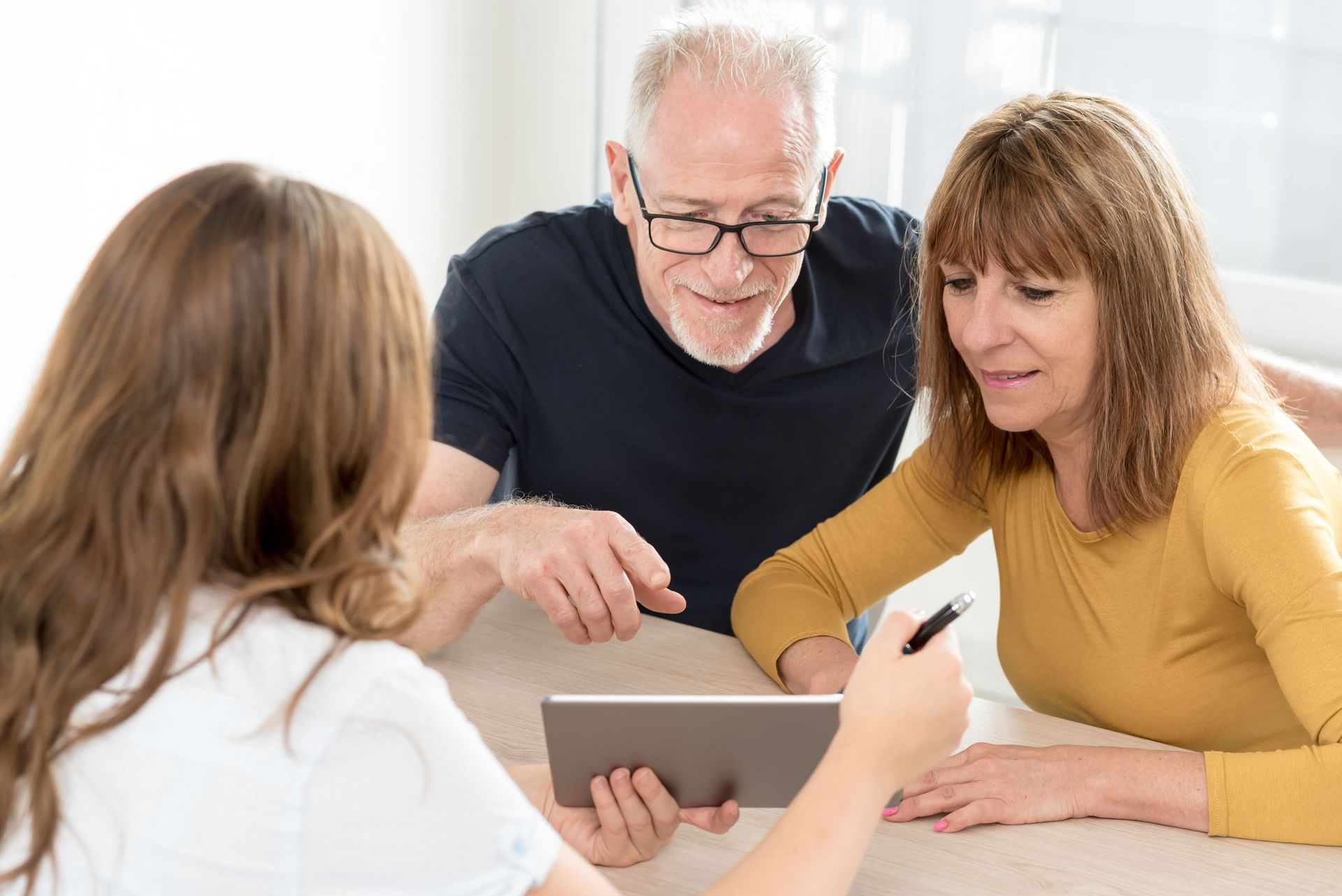 Woman showing tablet to couple seated at table.