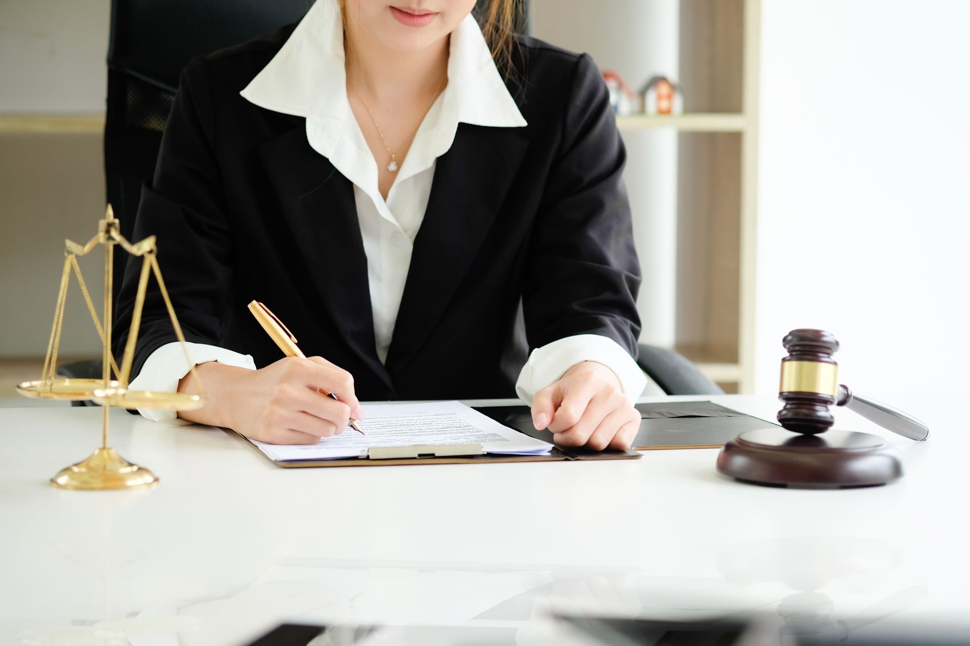 Lawyer in a black suit writing at a desk with a gavel and scales of justice.