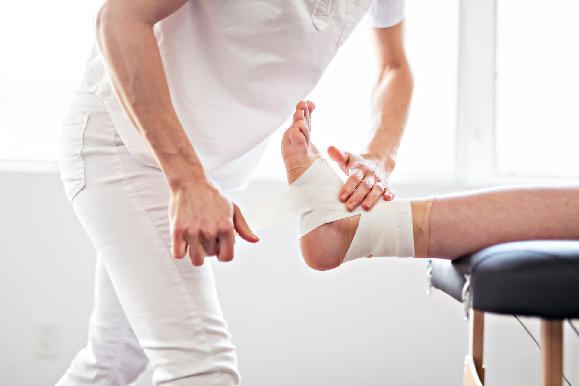 Person wraps white bandage around another person's ankle on a medical table.