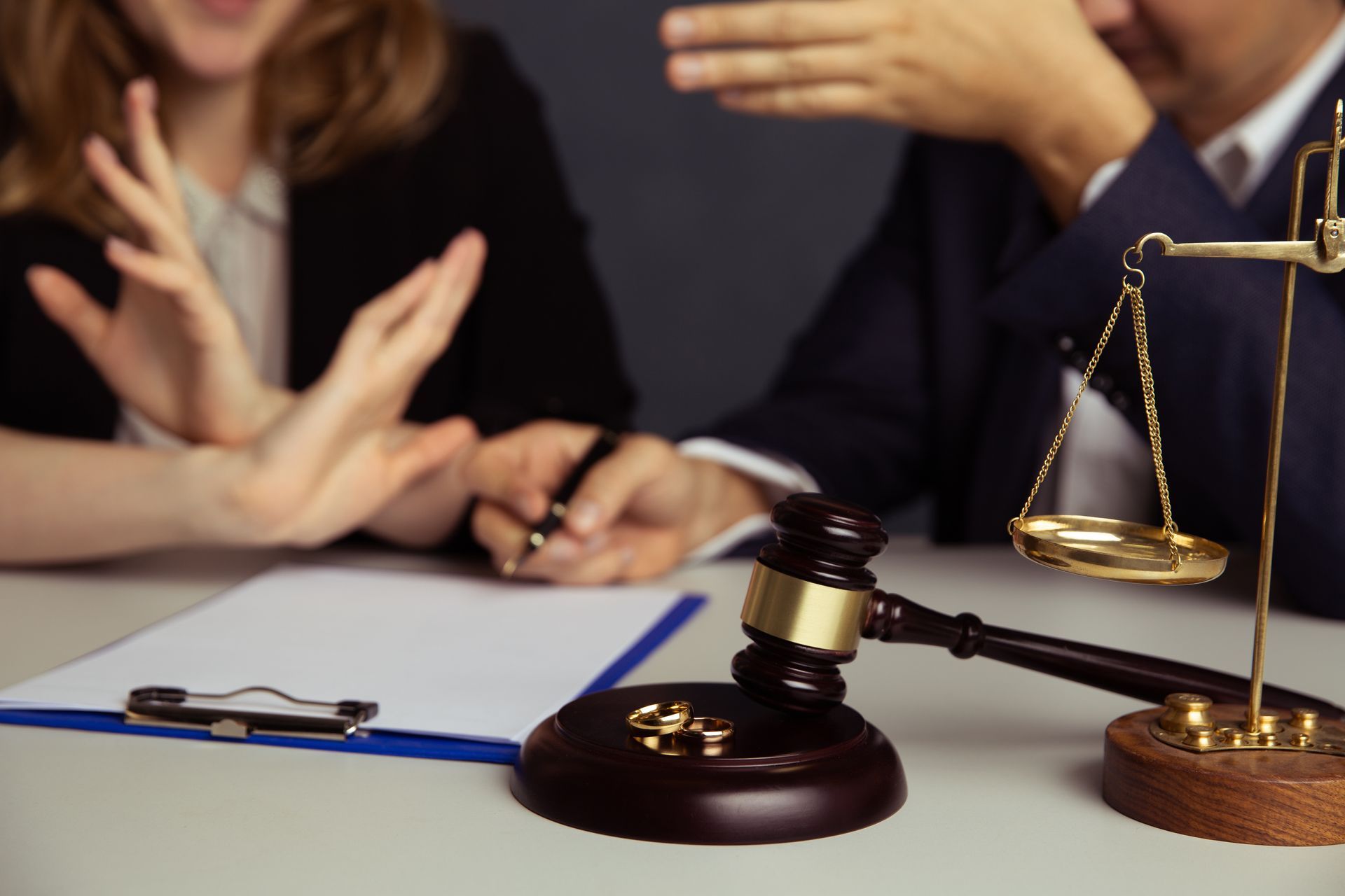 Judge's gavel and scales of justice on a desk with a couple in a legal dispute, one gesturing with hands.
