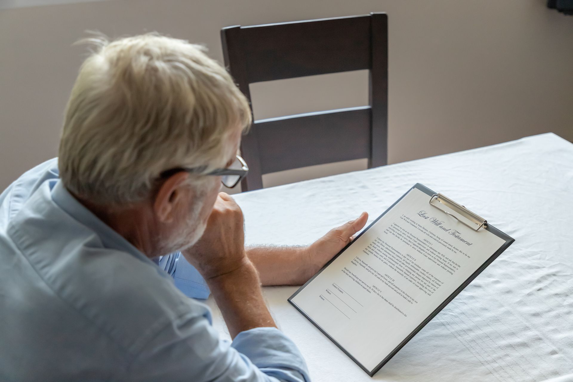 Man wearing glasses reads document on a clipboard, sitting at a table.