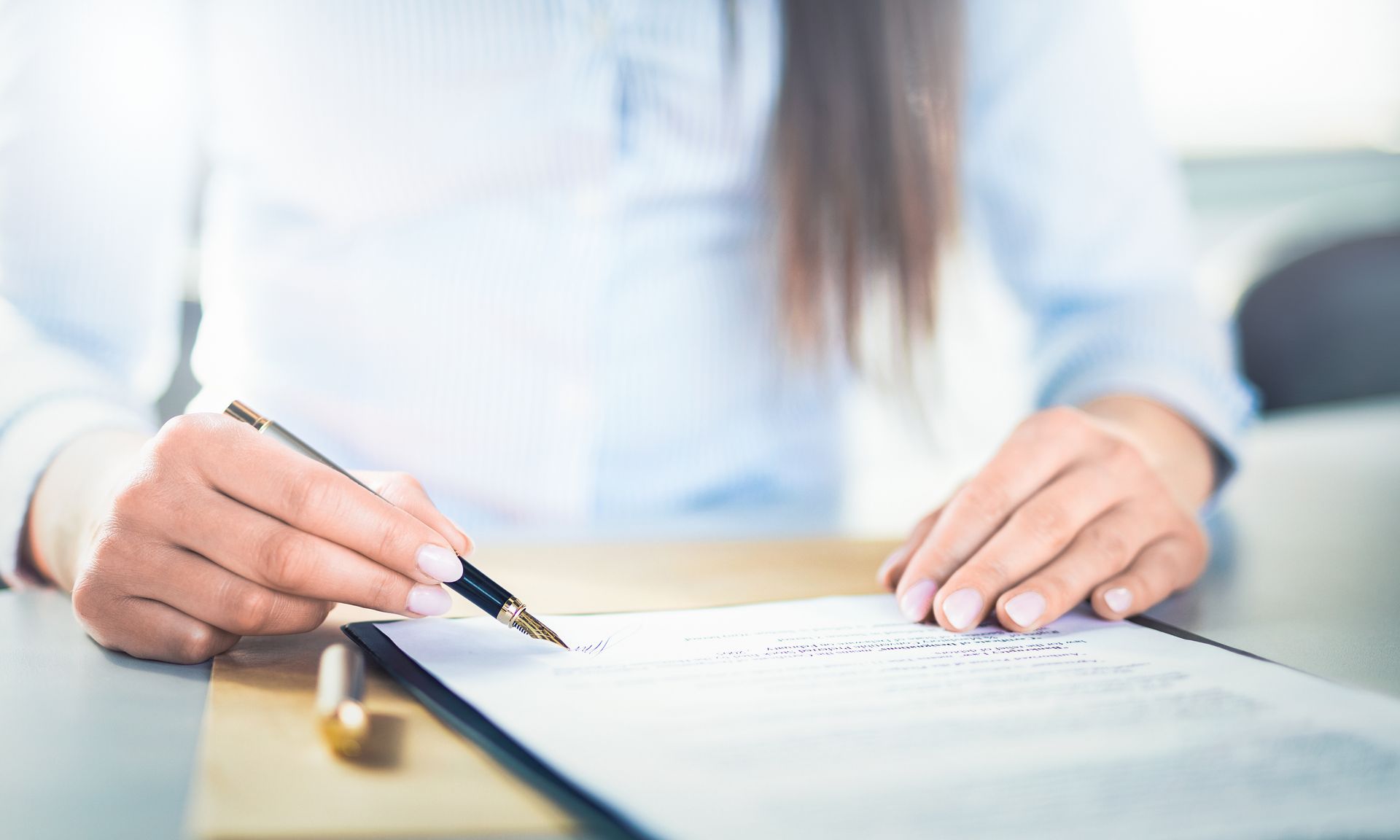 Woman's hands holding a pen, signing a document on a clipboard at a desk.