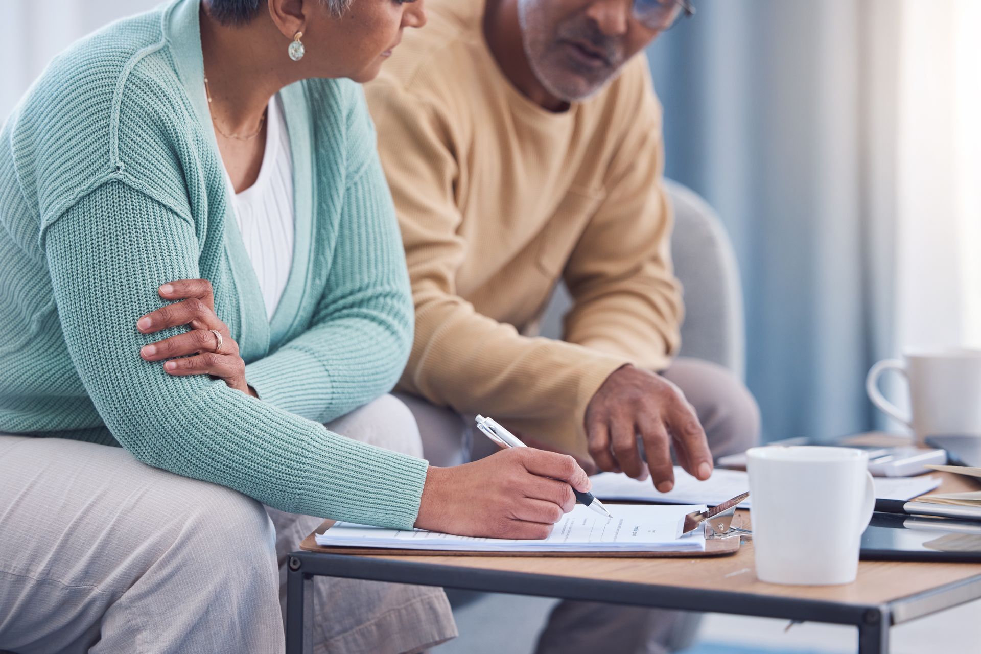 Couple reviewing documents together, one writing on a clipboard, sitting near a coffee table.