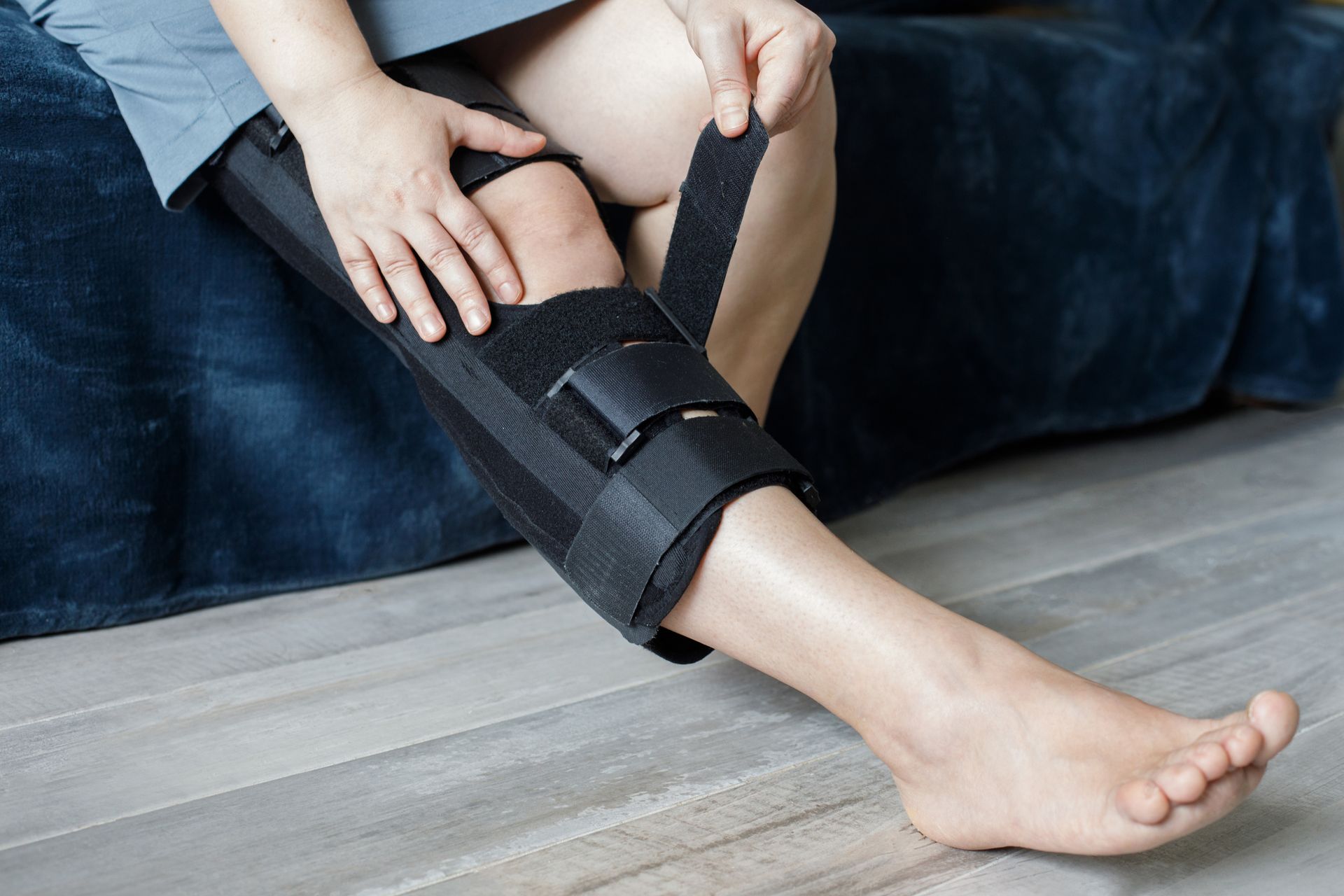 Person adjusting a black knee brace on their leg, sitting indoors.