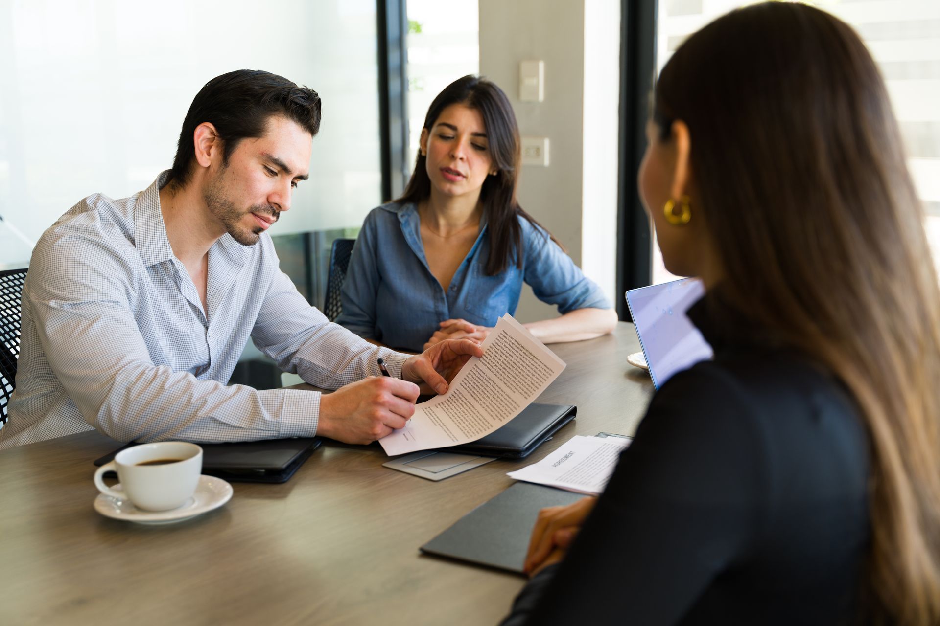 Couple signing documents with a professional at a table in an office setting.