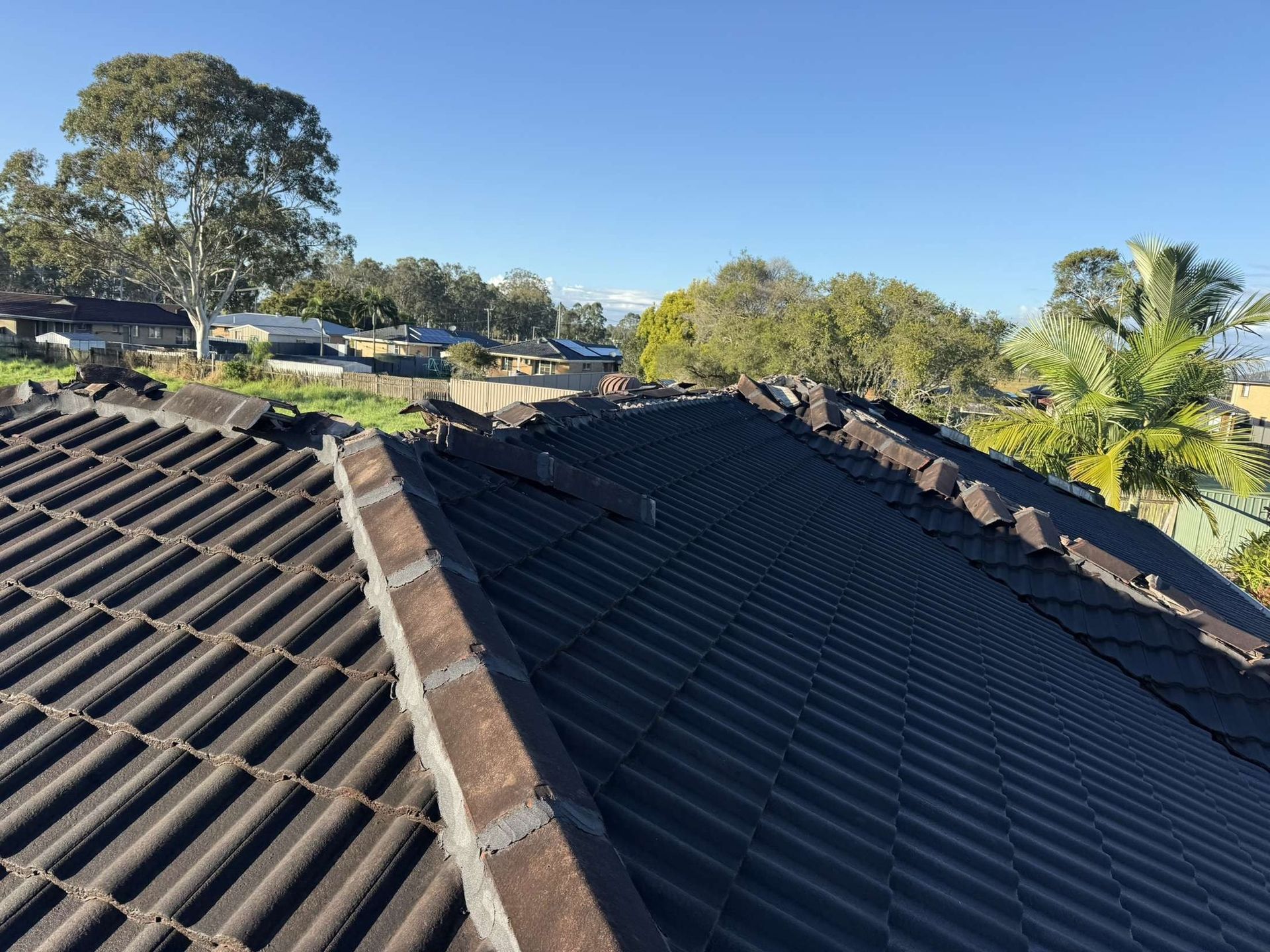 Rooftop with dark tiles, brick edging, and trees under a blue sky