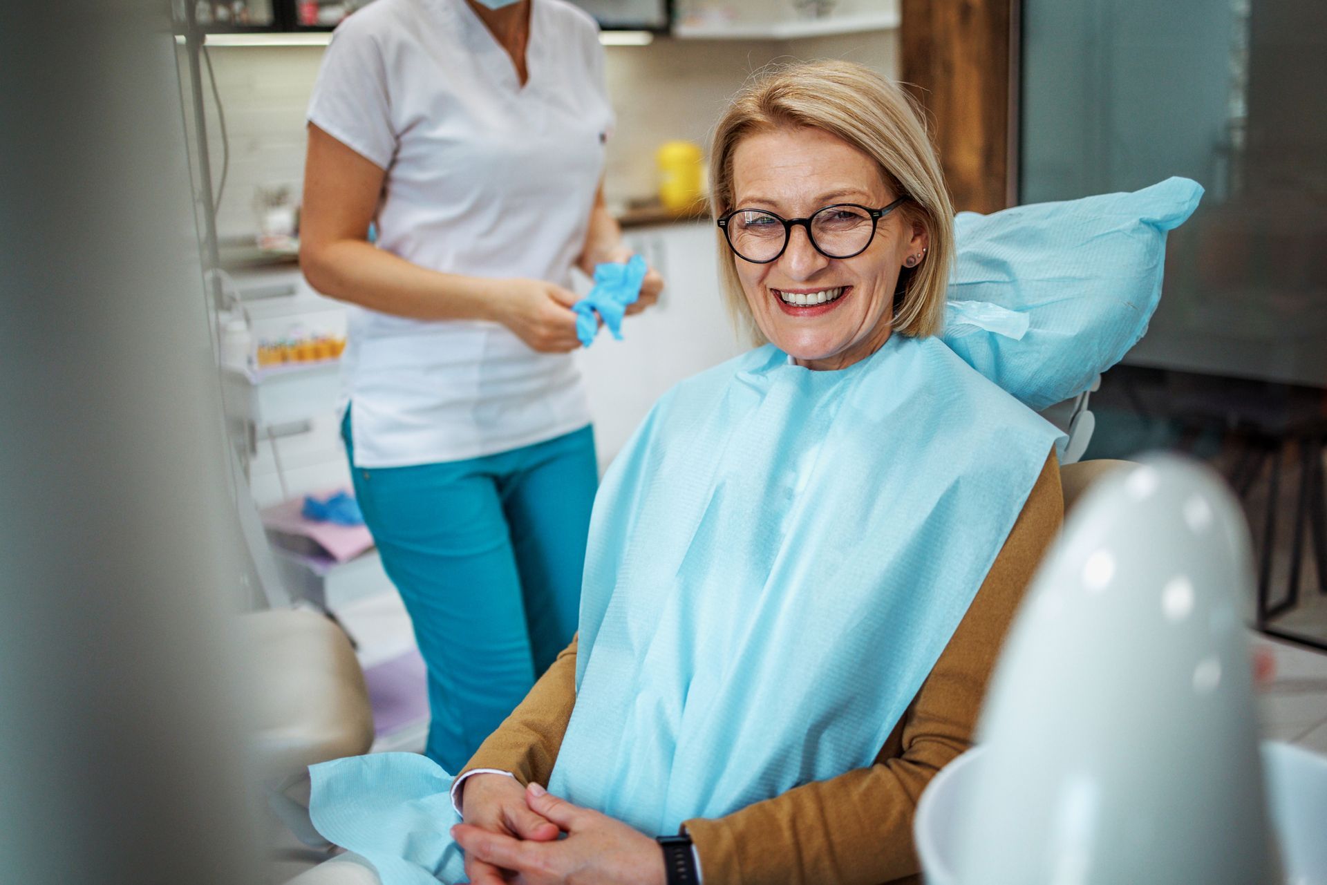 A woman is smiling while sitting in a dental chair.