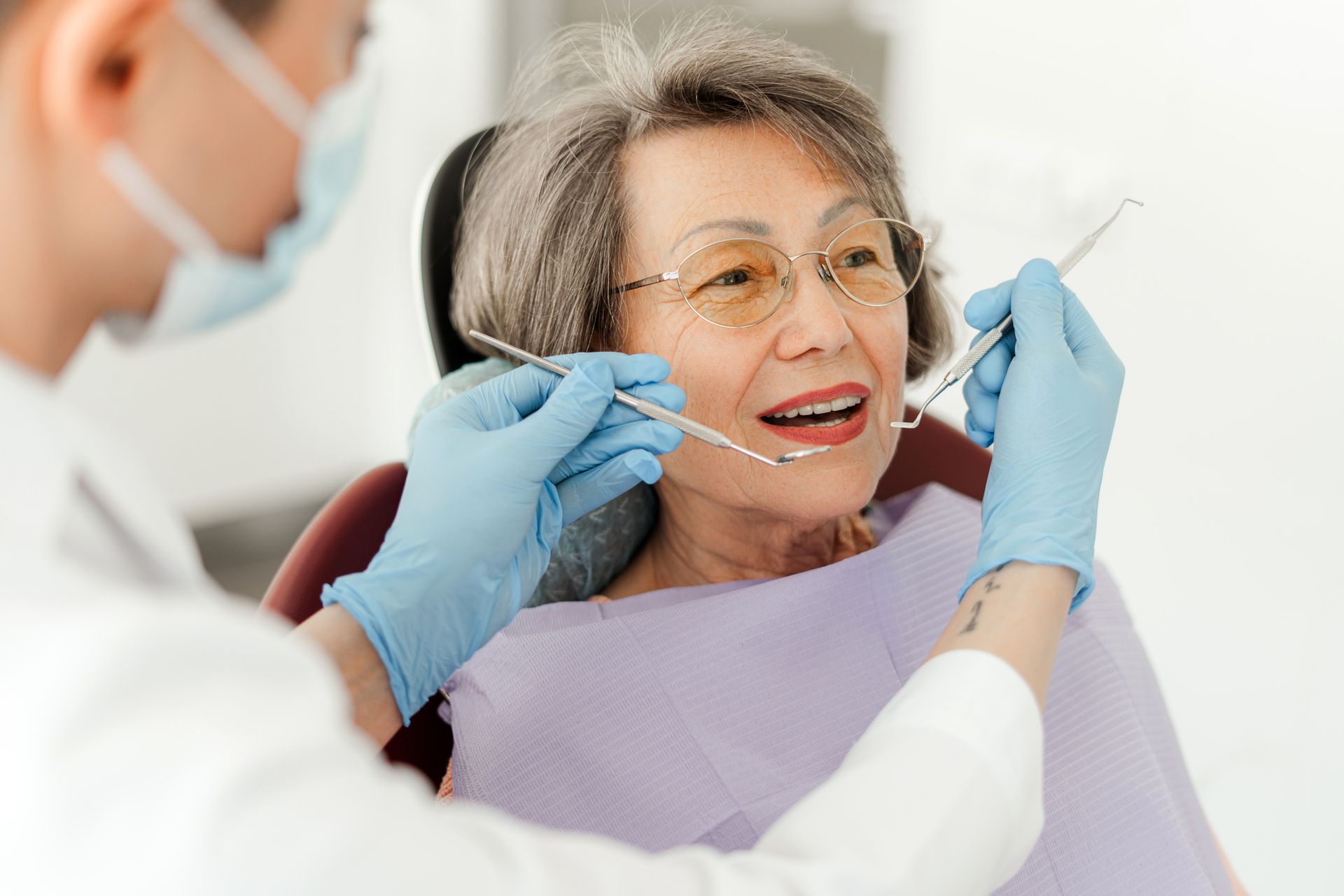 An elderly woman is sitting in a dental chair while a dentist examines her teeth.