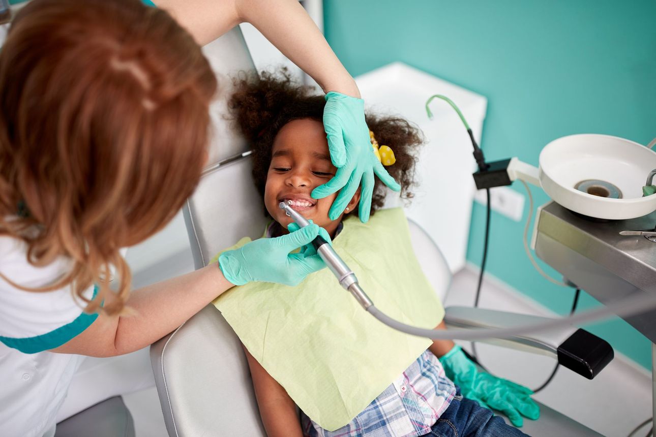 A little girl is sitting in a dental chair getting her teeth examined by a dentist.