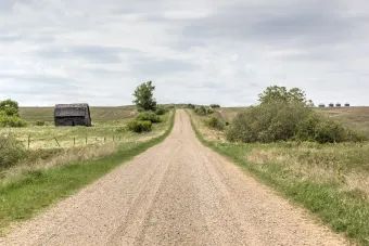 A dirt road going through a grassy field with a barn in the distance.