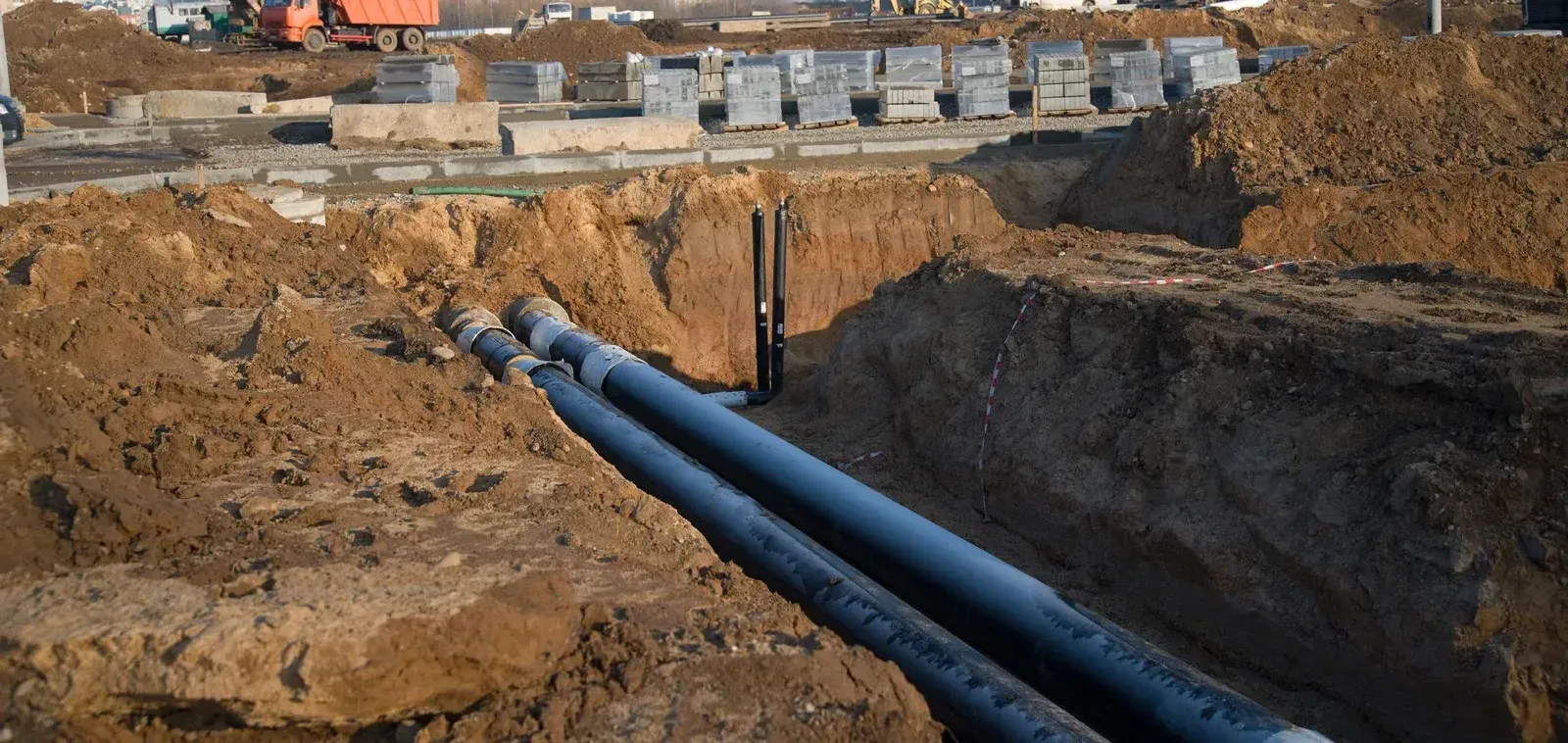 A bunch of pipes are laying in the dirt on a construction site.