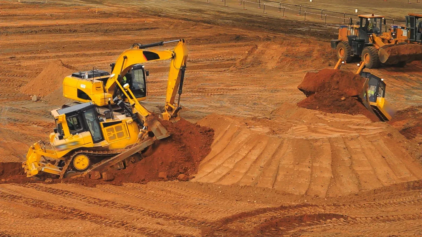 A bulldozer and an excavator are working on a dirt field.
