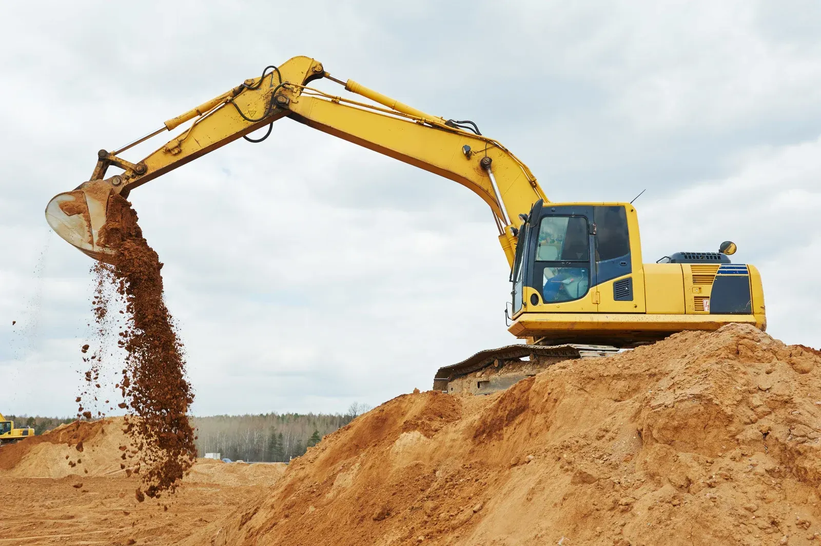 A yellow excavator is pouring dirt into a pile of dirt.