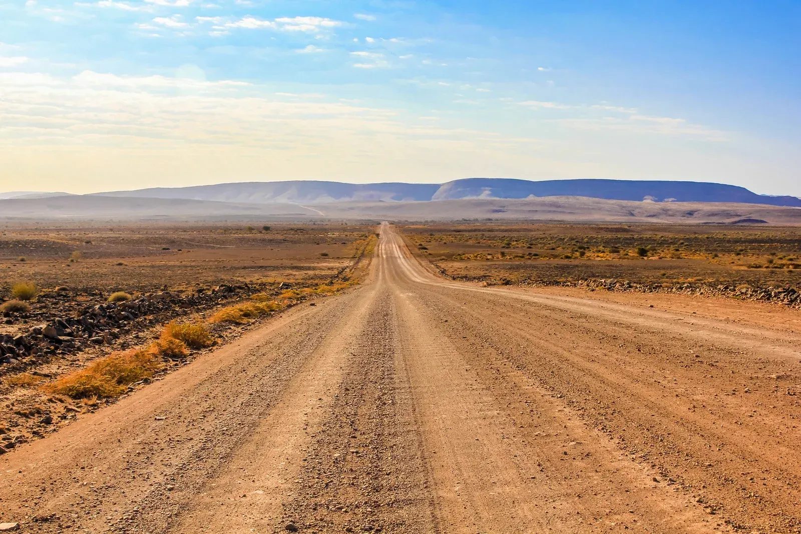 A dirt road in the desert with mountains in the background.