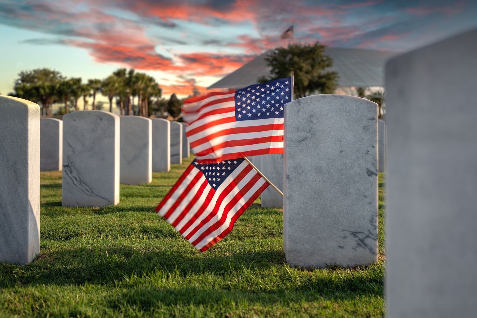 American flags in a cemetery at sunset, with rows of gravestones and a colorful sky