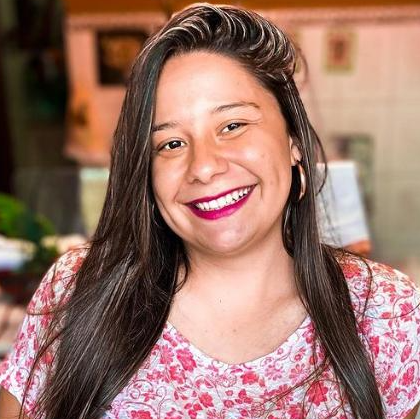 Uma mulher de cabelos longos está sorrindo e vestindo uma camisa rosa.