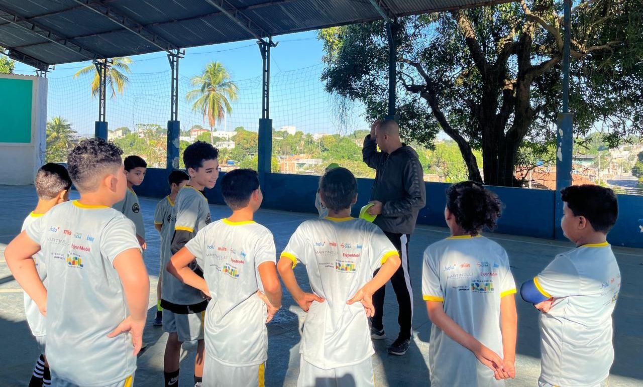 Um grupo de crianças está em pé, formando um círculo, com as mãos na cintura.
