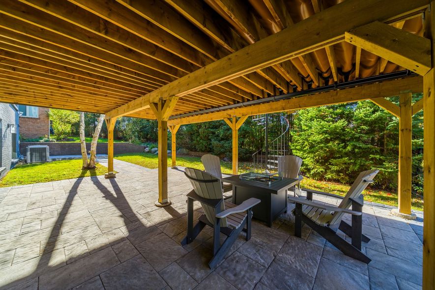 Covered patio with seating area, stone flooring, and lush green backyard.