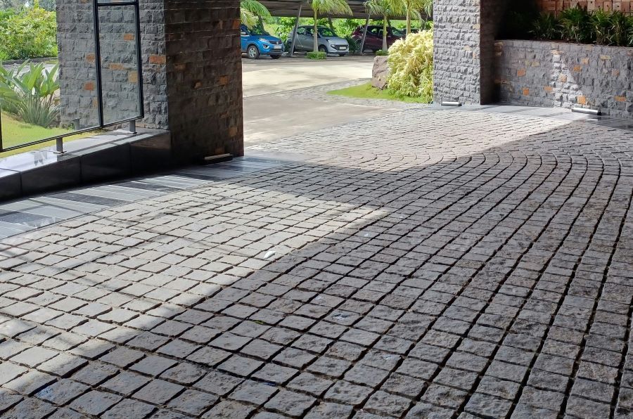 A brick driveway with cars parked in the background.