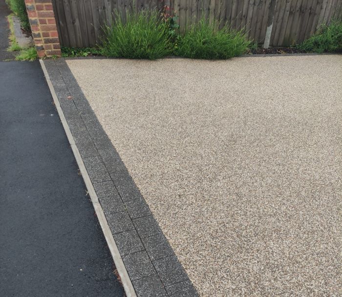 A driveway with a black curb and a brick fence in the background.