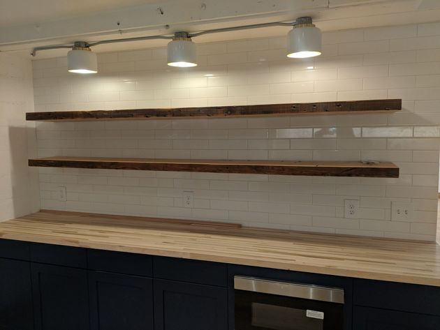 Modern kitchen with white tile backsplash, two wooden shelves, pendant lights, and dark cabinets