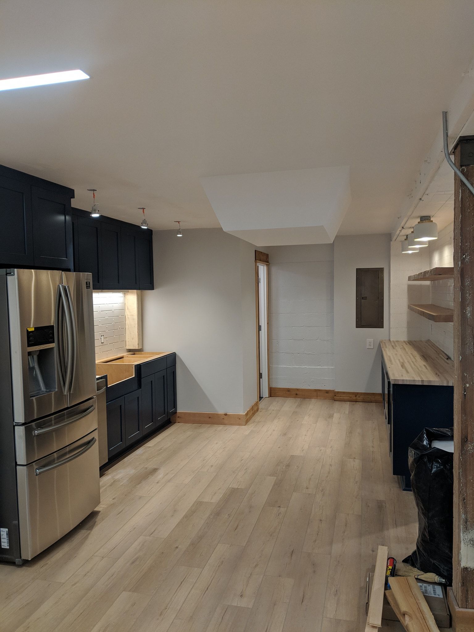 Kitchen renovation in progress: blue cabinets, stainless steel fridge, light wood floors, exposed beams, and unfinished areas.