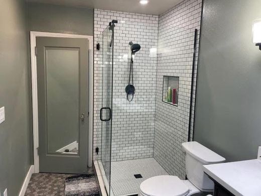 A bathroom featuring a glass-enclosed shower with white subway tiles, a toilet, a vanity, and a gray door.