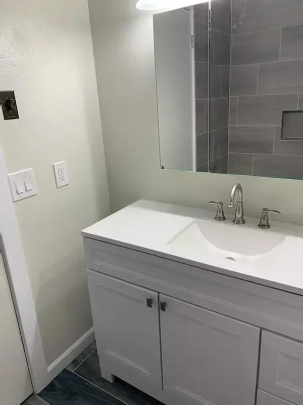 White bathroom vanity with sink, mirror, and gray tiled shower.