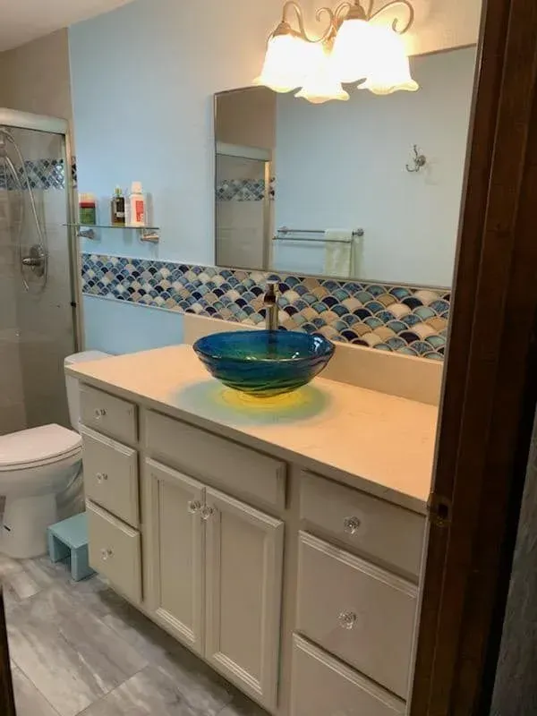 Bathroom with blue and yellow vessel sink, white vanity, blue tiled backsplash.