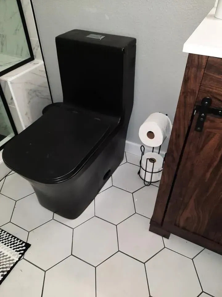 Black toilet in a bathroom with white hexagonal tile flooring, a wooden vanity, and a black toilet paper holder.