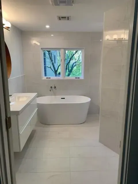 Modern bathroom with white walls, tub, and vanity; natural light through window.
