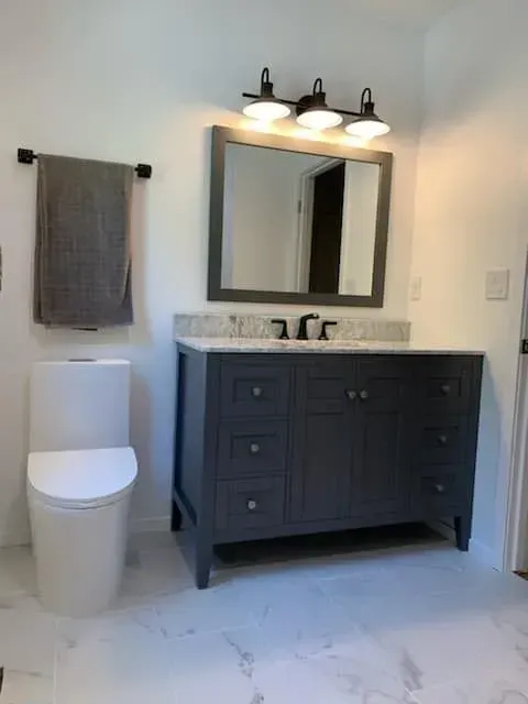 Bathroom with gray vanity, white toilet, marble-look floor, and black fixtures.