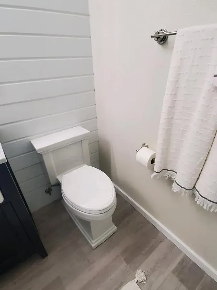 A small white bathroom with a toilet, shiplap wall, towel rack with towel, and gray flooring.