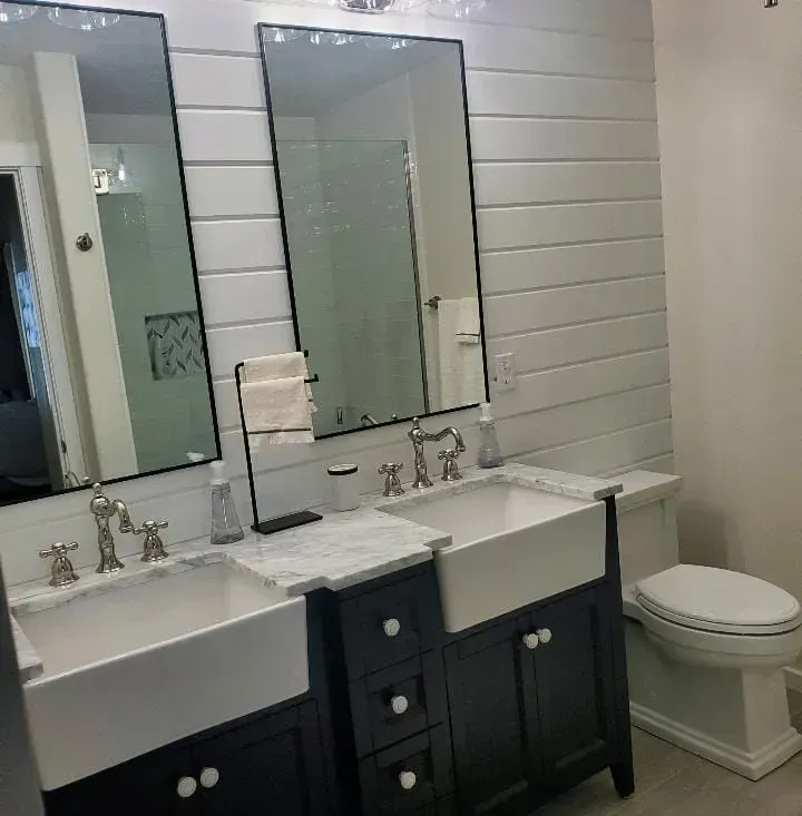 Bathroom with white shiplap walls, dual sinks, large mirrors, dark blue cabinets, and a white toilet.