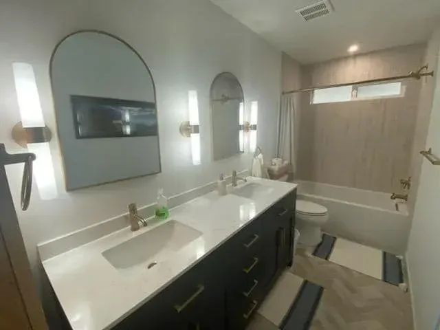 Bathroom with double vanity, arched mirrors, gold fixtures, and a bathtub.