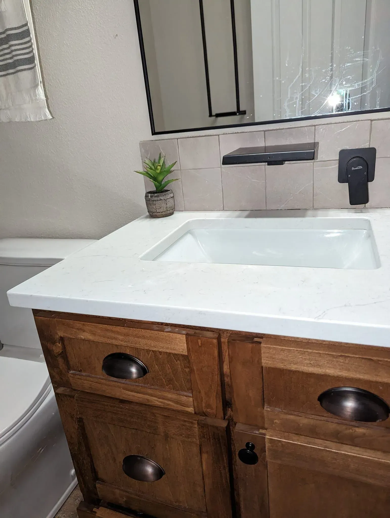 Bathroom vanity with a wood cabinet, white countertop, and rectangular sink.