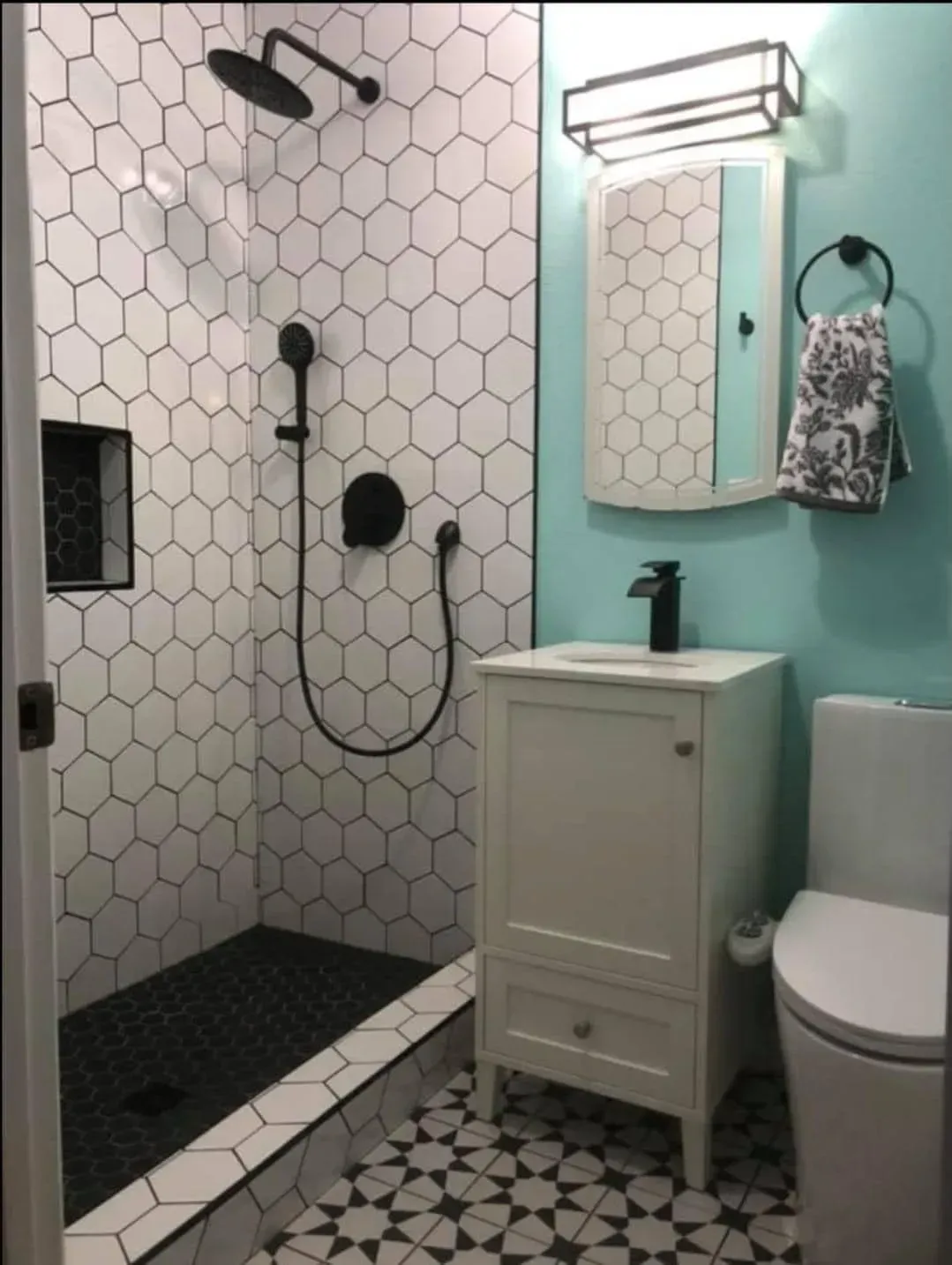 Bathroom with white hexagonal shower tiles, black shower fixtures, and turquoise wall.