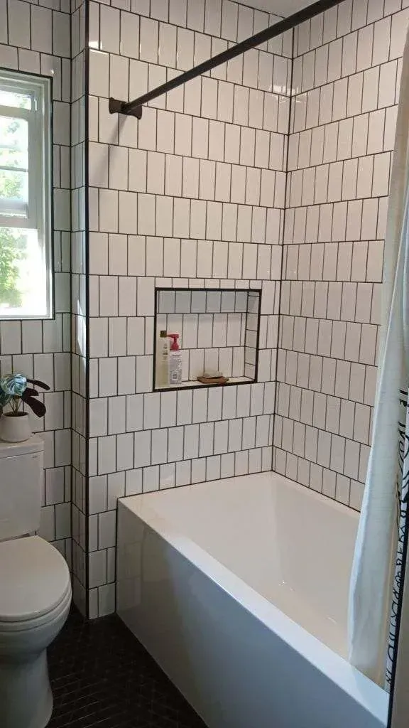 A modern bathroom with white rectangular tile. A toilet, bathtub, and shower curtain are present.
