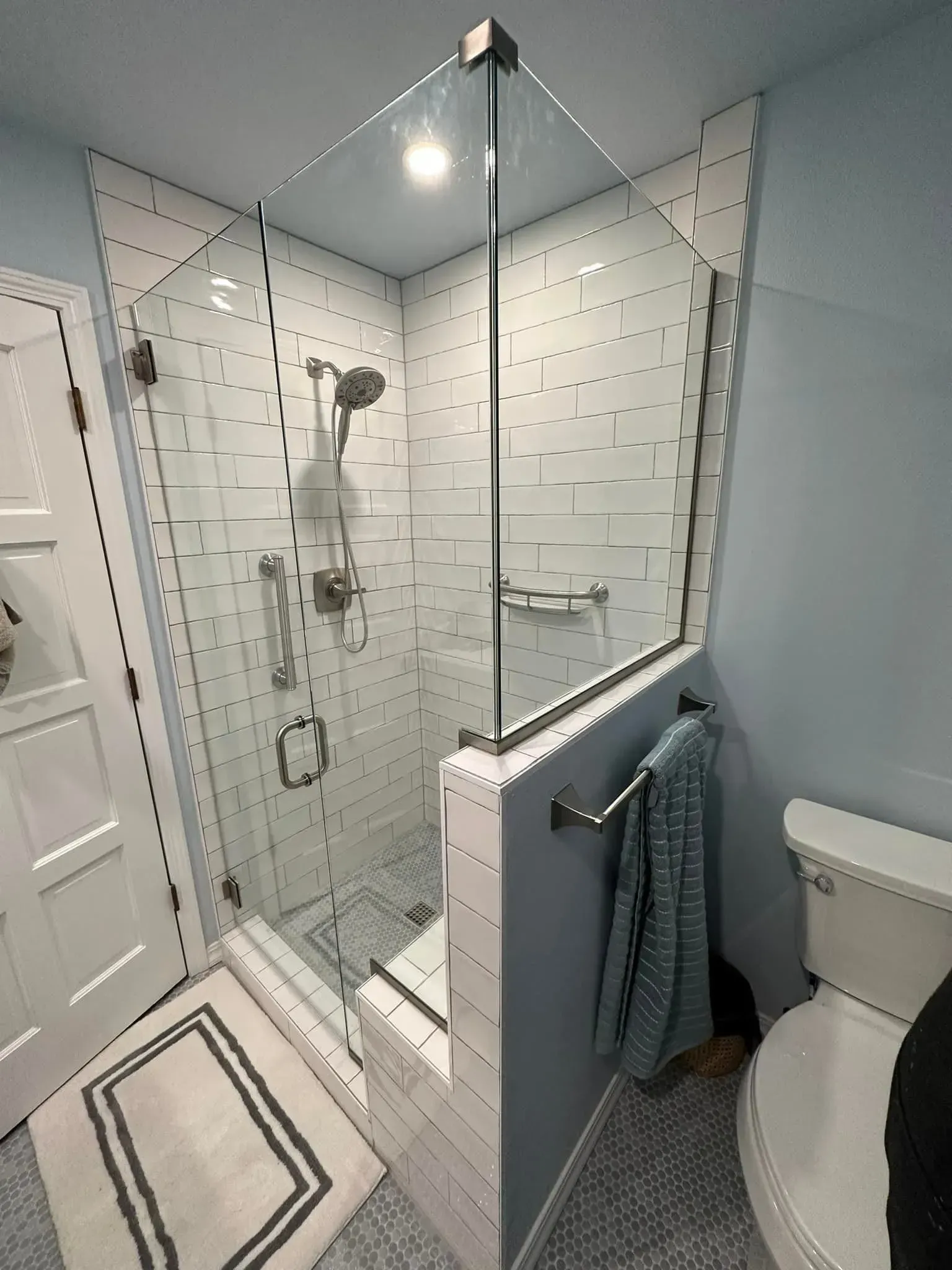Modern bathroom with glass-enclosed shower, white textured tile, chrome fixtures, and a toilet.