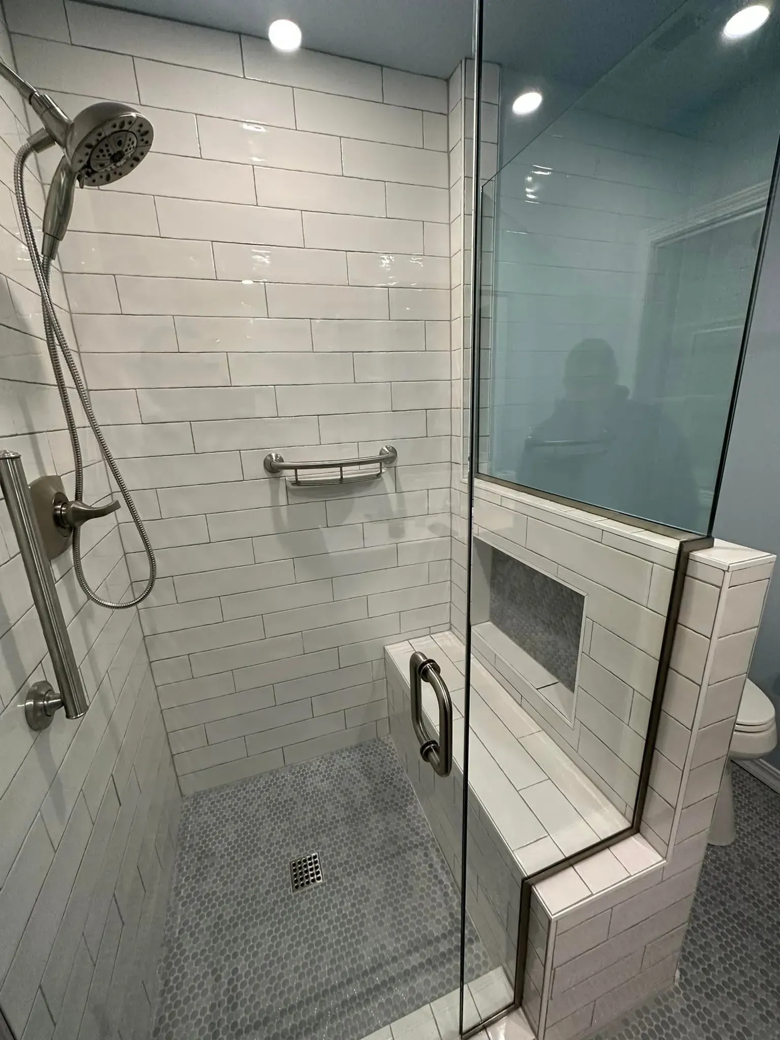 Shower with white tiled walls, glass door, and a built-in bench.