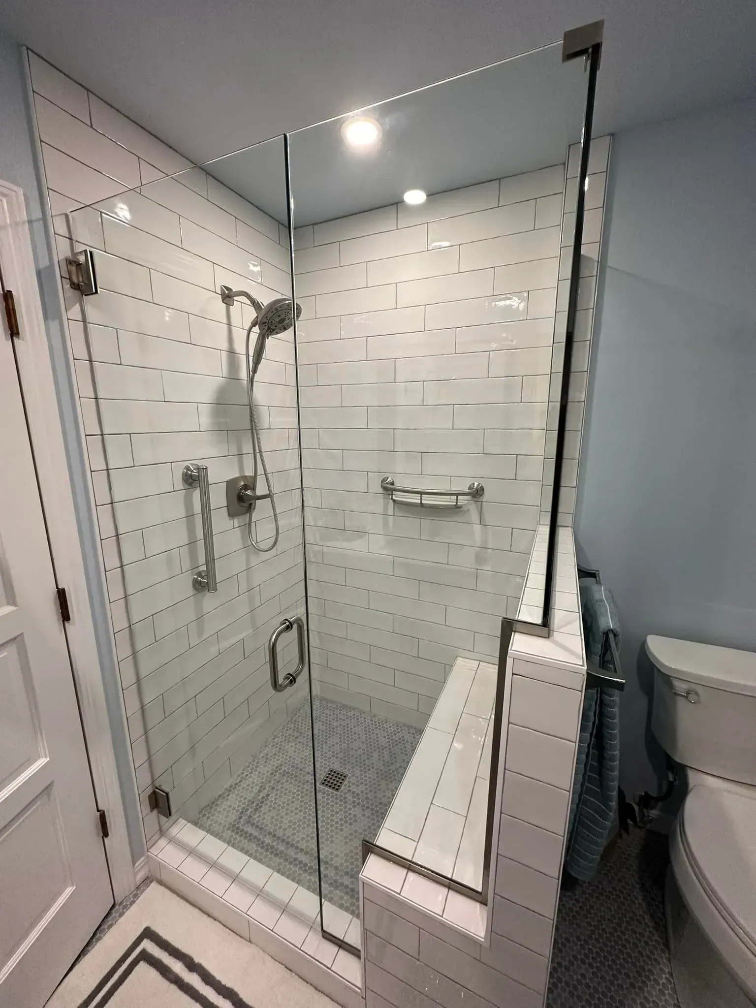 Glass shower enclosure with white tiled walls and a toilet.