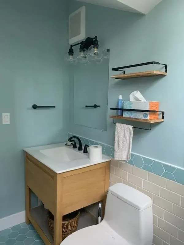 Bathroom with blue walls, wood vanity, and decorative shelves.