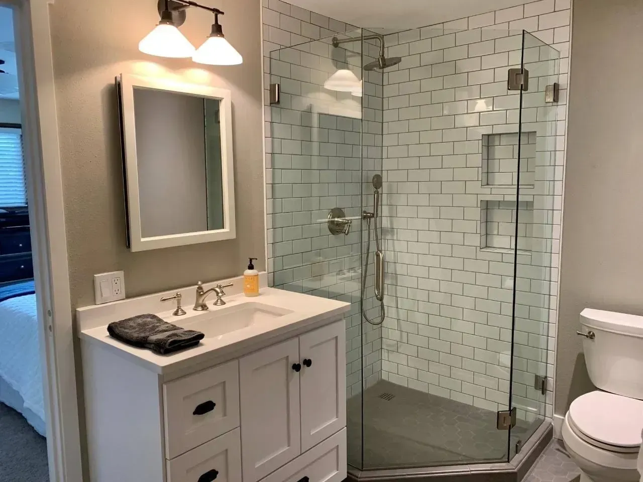 Bathroom with white vanity, framed mirror, glass shower with white tile, and a toilet.