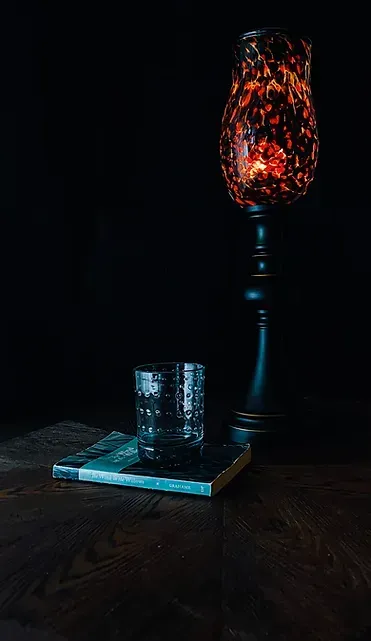 A lamp is sitting on a wooden table next to a book and a glass.