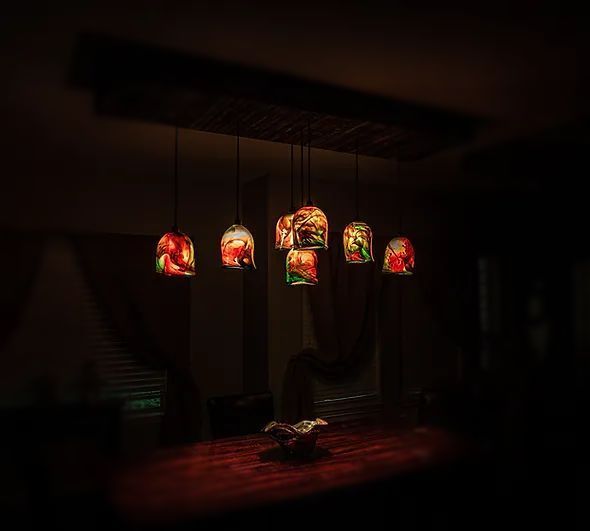 A dining room table with a bunch of stained glass lamps hanging from the ceiling.