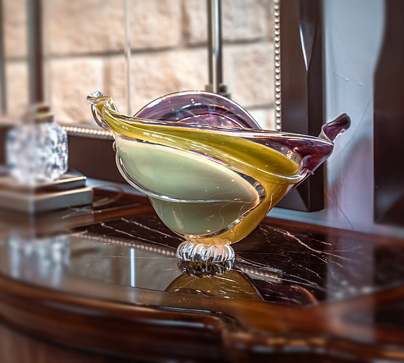 A colorful glass bowl is sitting on a table next to a mirror.