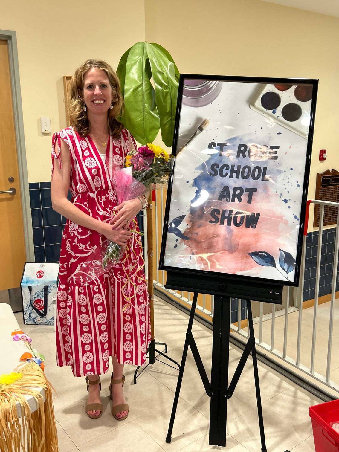 Art teacher Meg Ferriter poses next to the sign for the art show. She holds a bouquet of flowers.