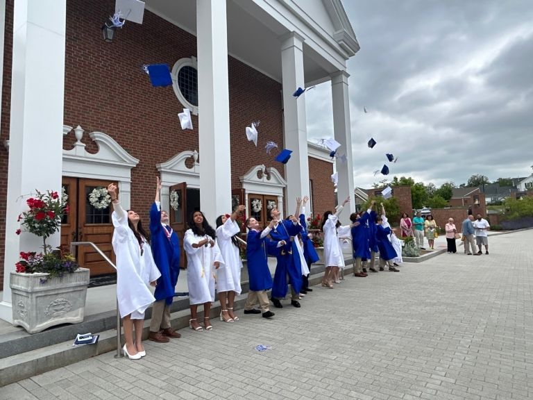 Image shows the 8th grade students from the Class of 2023 in blue and white gowns, tossing their mortar board caps in the air